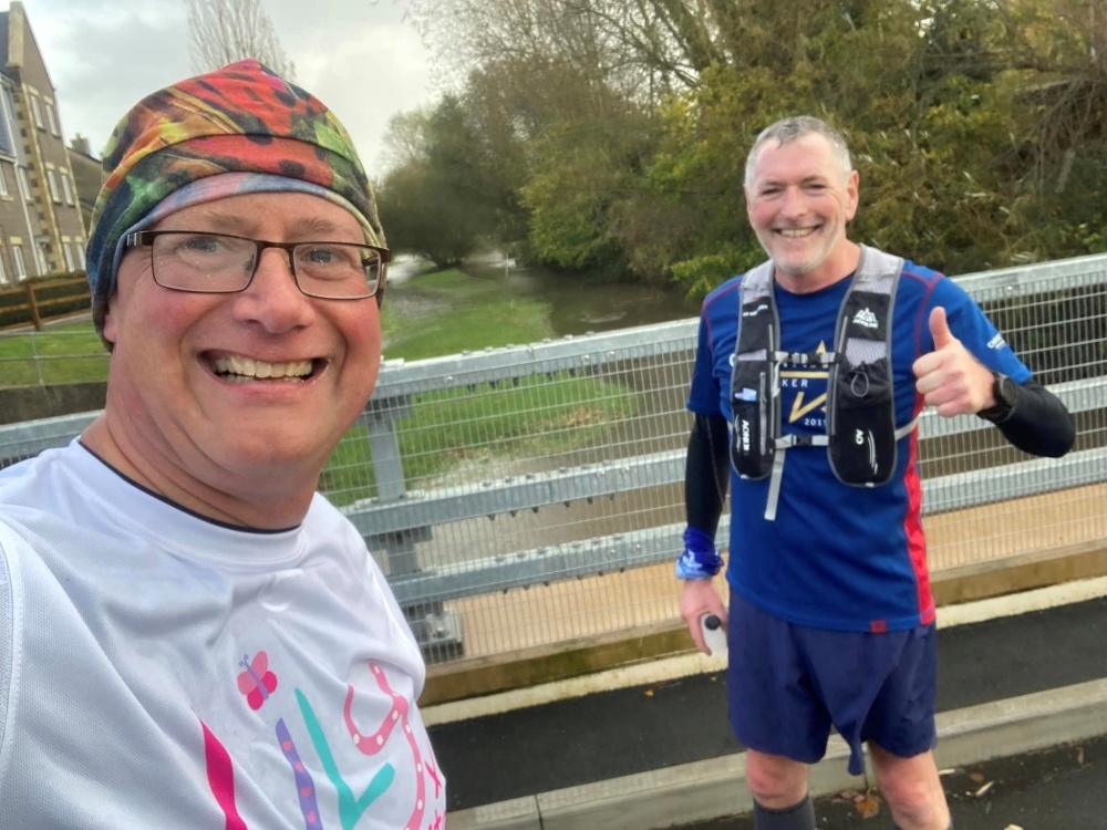 Two runners on a bridge smiling at the camera