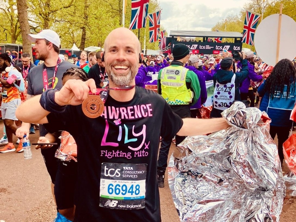 A man in a Lily Foundation top smiling and holding up his London Marathon finishers medal