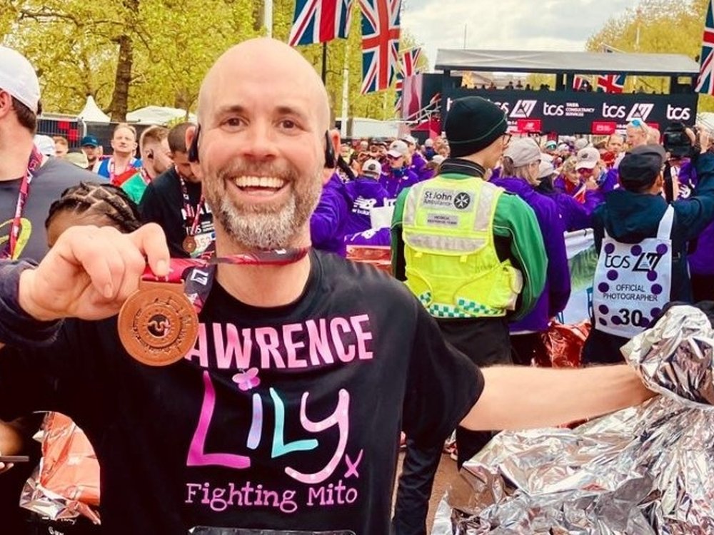 A man in a Lily Foundation t-shirt smiling and holding up his London Marathon finishers medal